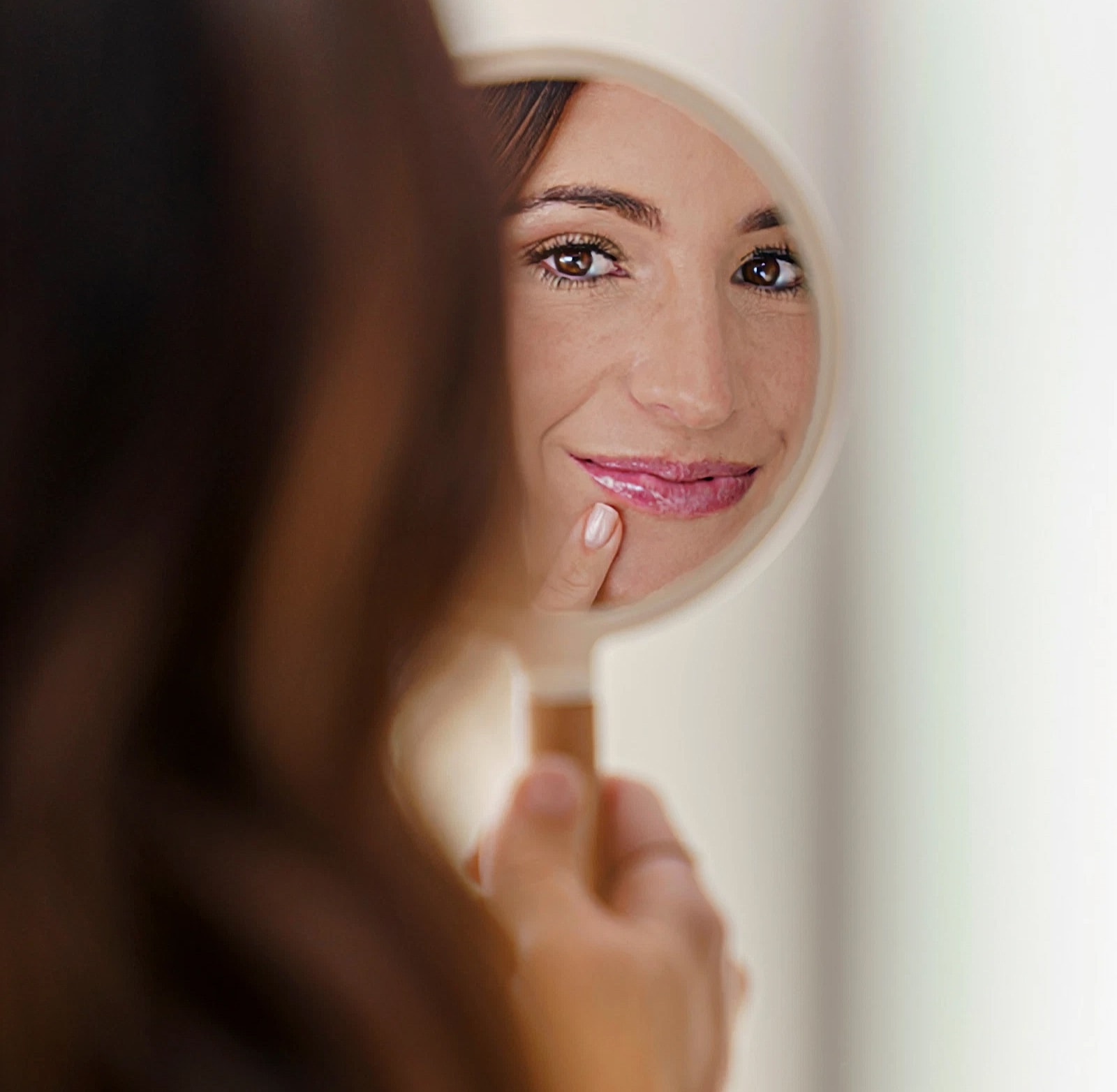 Woman smiling in mirror, touching her chin.